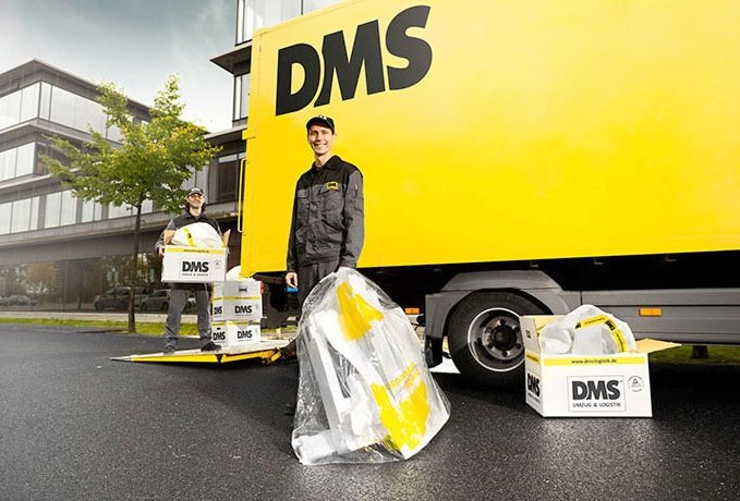 DMS-Mitarbeiter mit Umzugskartons vor einem DMS-Lkw
